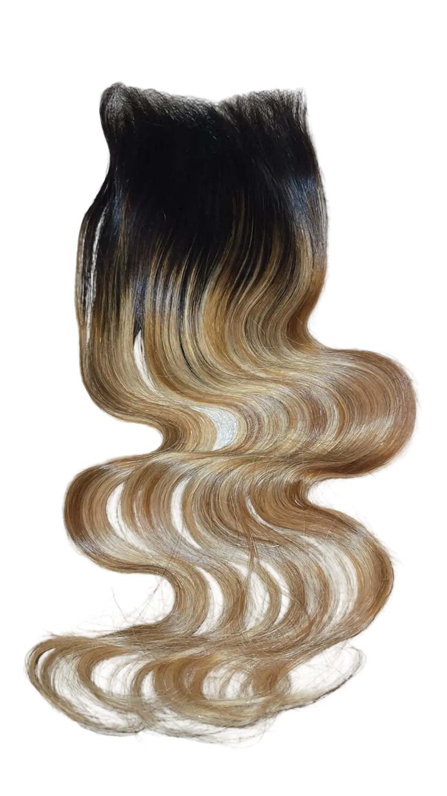 A wavy hair extension piece with a dark black top transitioning into warm golden blonde and light brown tones, laid flat on a textured beige surface.